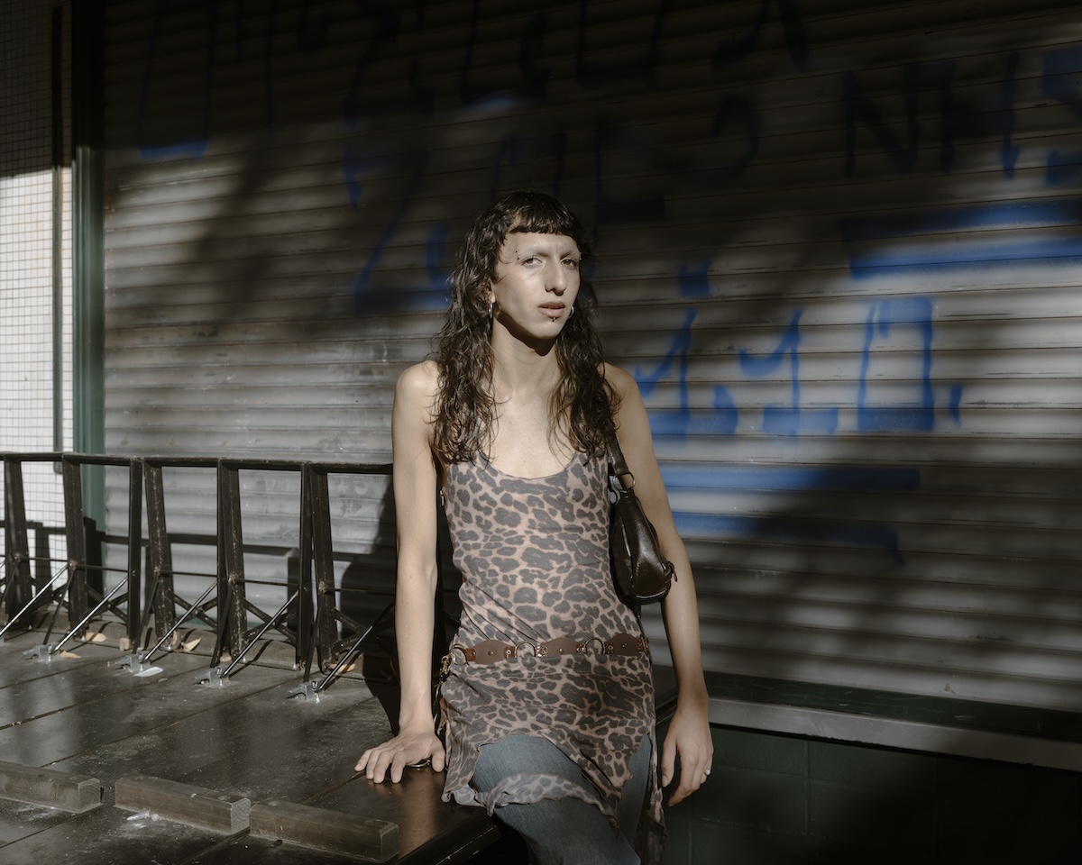 A person in a leopard print dress posing in front of a wall with a graffiti on it