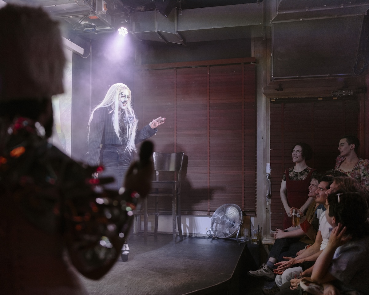 Photo of a person in drag makeup performing before an audience