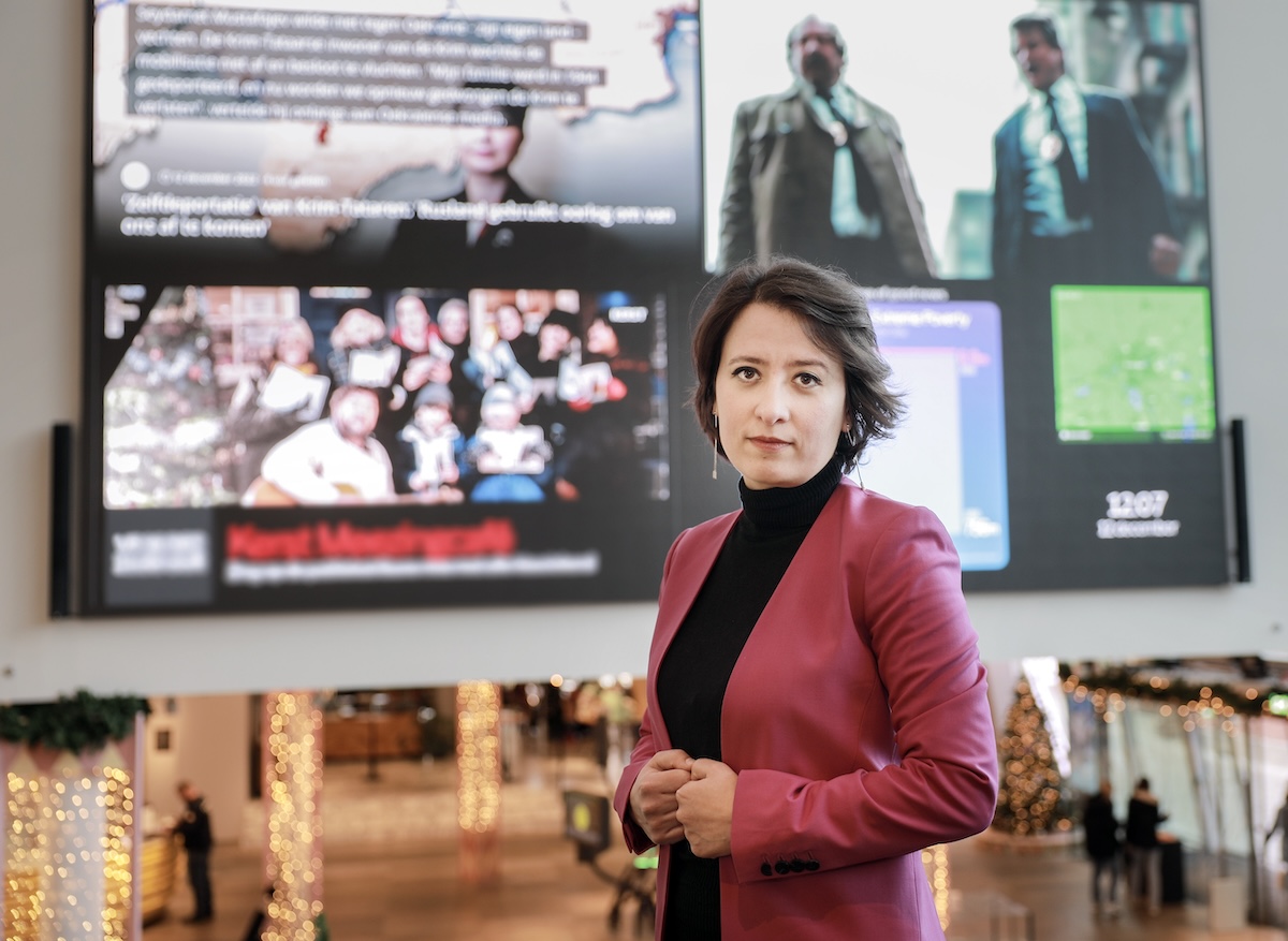 Woman in black sweater and crimson jacket poses for a photo in a spacious hallway