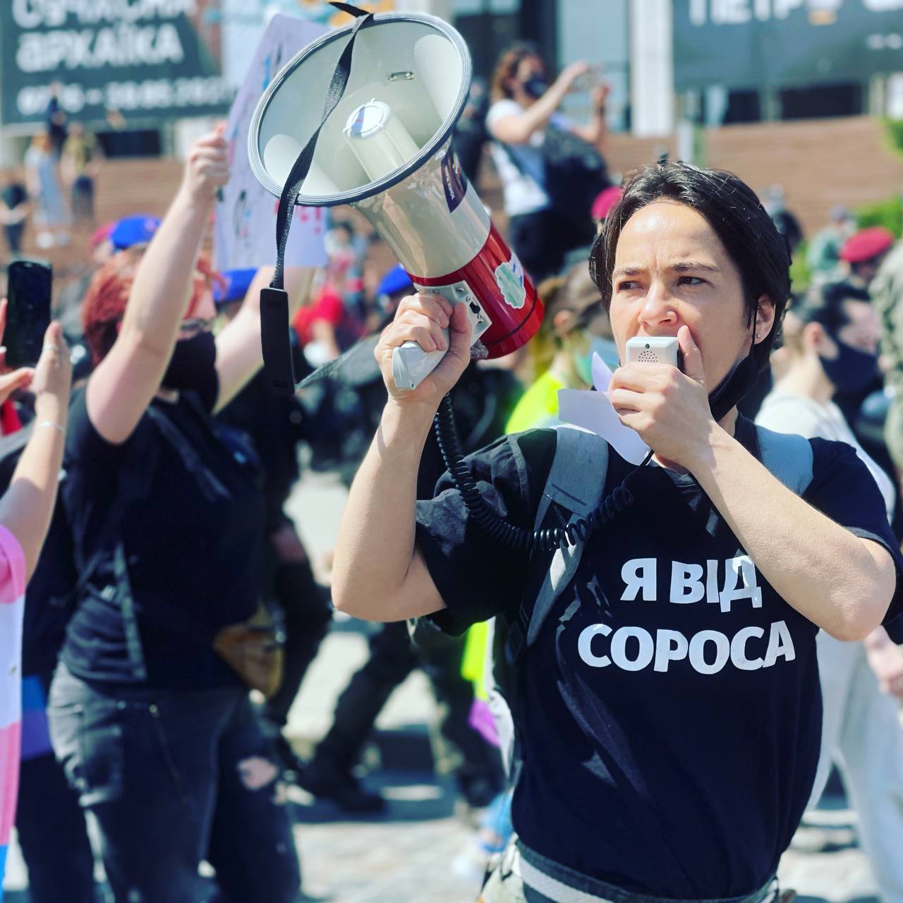 A person with a loudspeaker in a sweatshirt saying "I'm from Soros" in Ukrainian