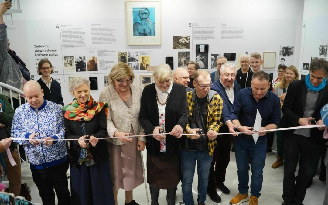 People are standing at a pink ribbon at a museum opening and cutting it to celebrate.