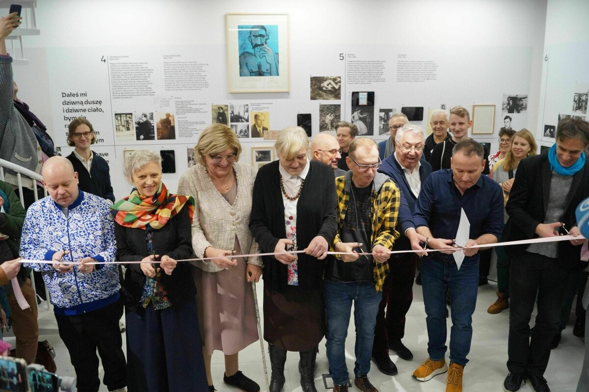 People are standing at a pink ribbon at a museum opening and cutting it to celebrate.